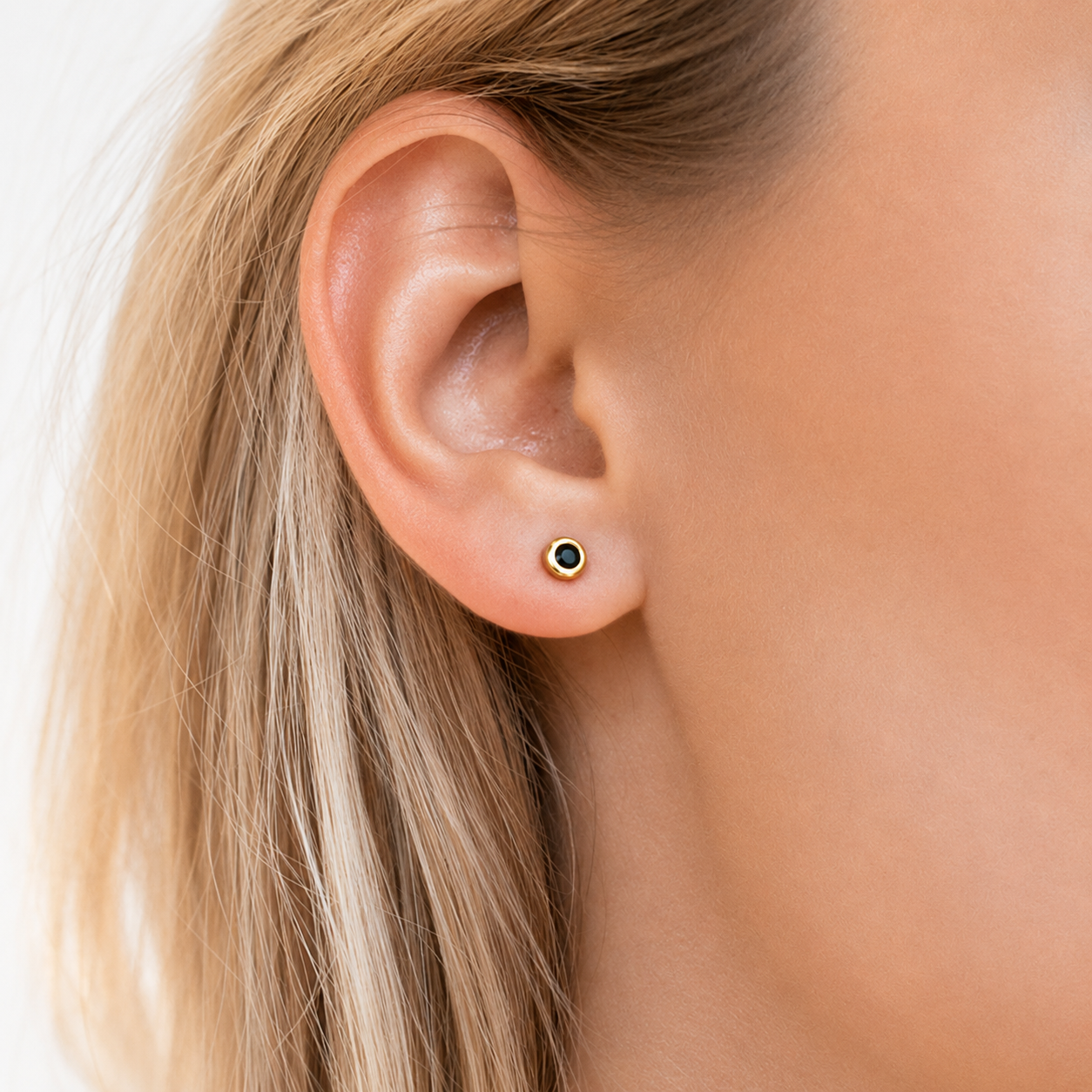 Close-up of an ear wearing a black and gold stud earring on a white background