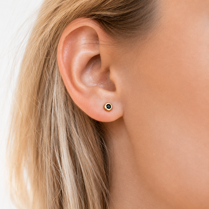 Close-up of an ear wearing a black and gold stud earring on a white background