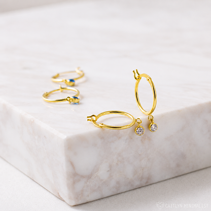 Gold hoop earrings with small gemstones on a marble surface