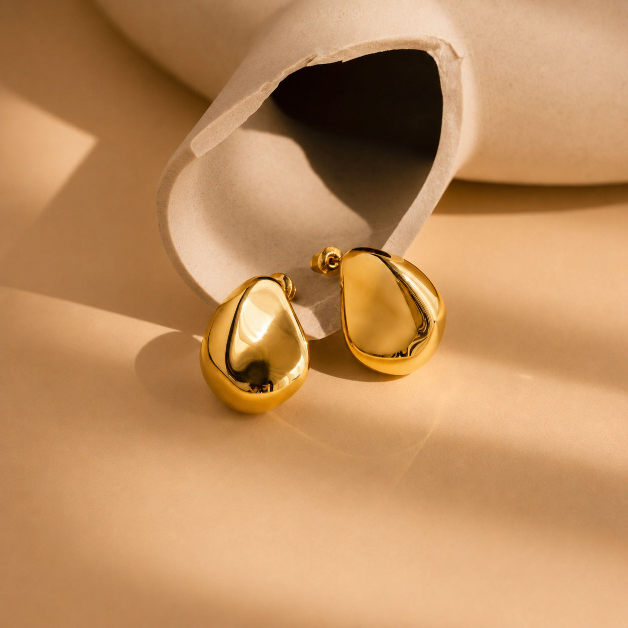 Gold teardrop earrings on a beige surface with a white container.