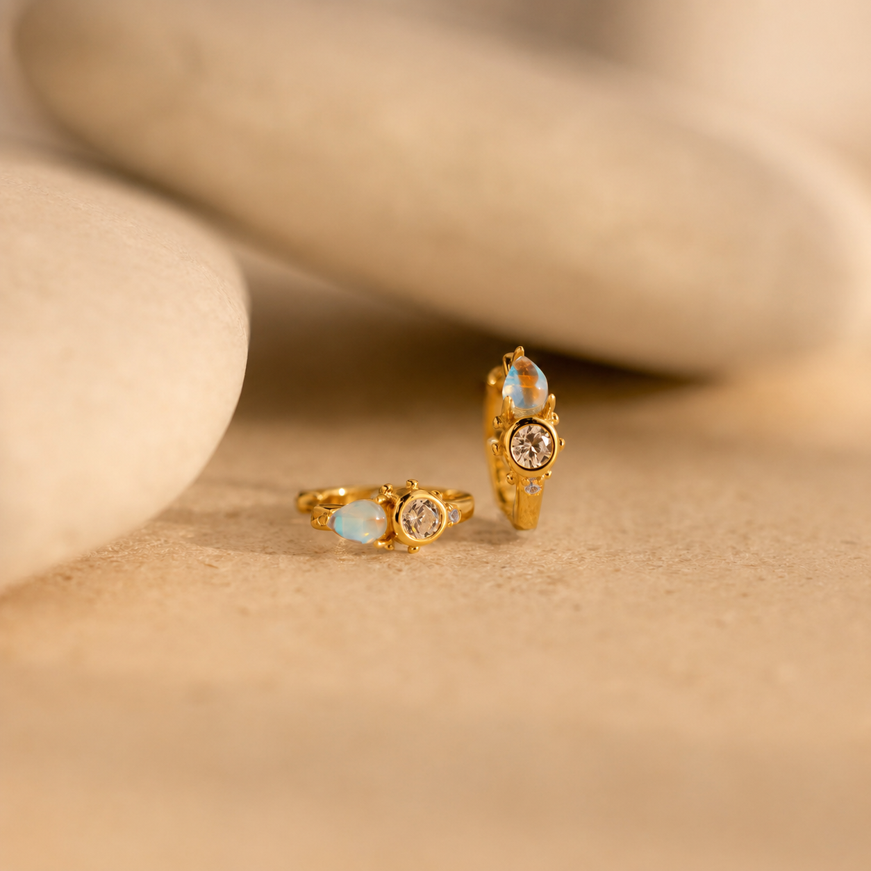 Gold earrings with gemstones on a beige surface