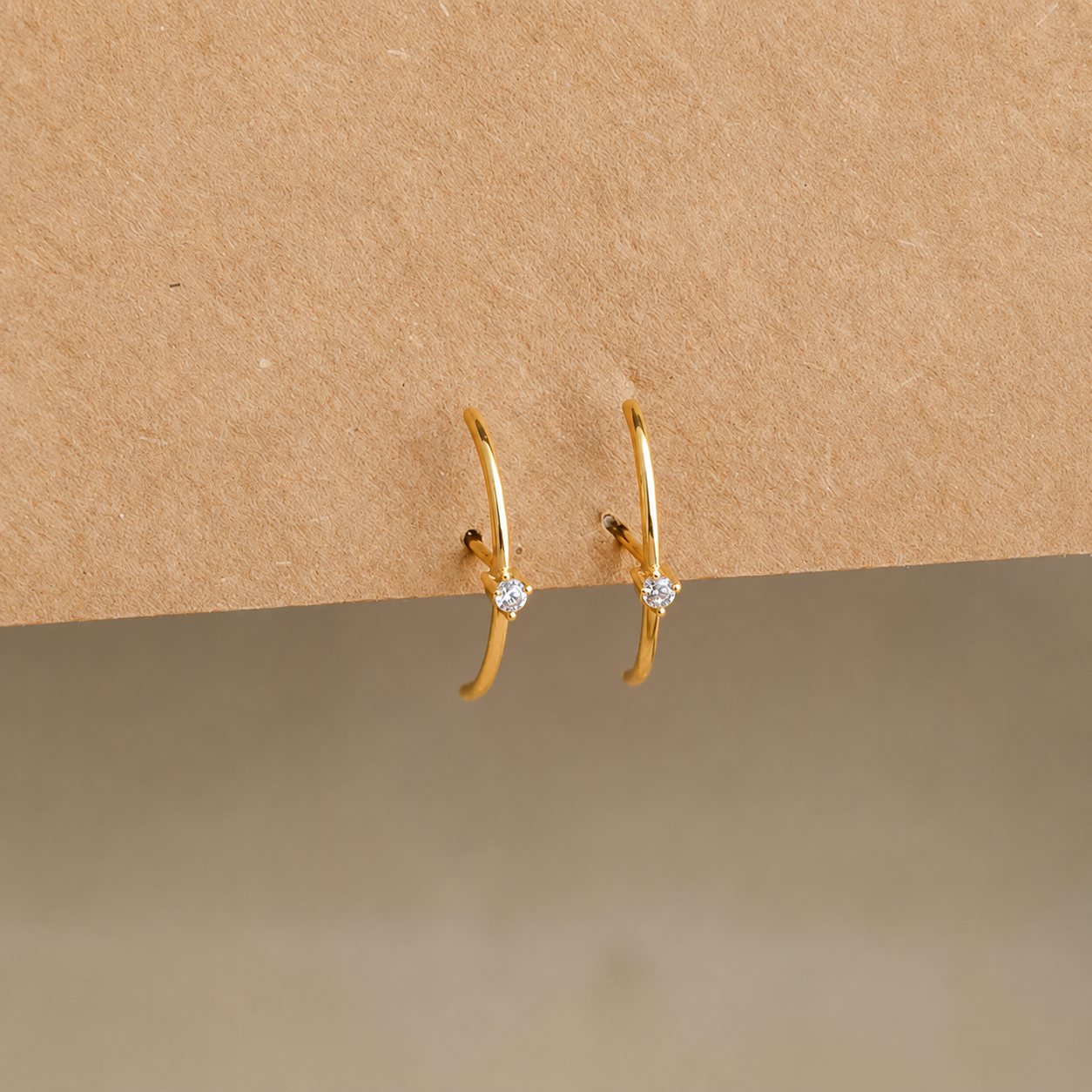 Gold hoop earrings with small diamonds on a beige background