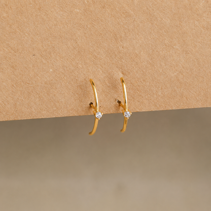 Gold hoop earrings with small diamonds on a beige background