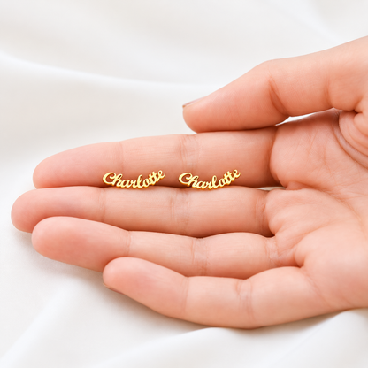 Gold 'Charlotte' earrings held in a hand on a white background