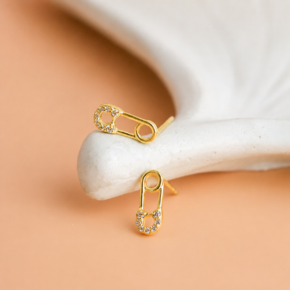 Gold safety pin earrings on a white stone with a beige background
