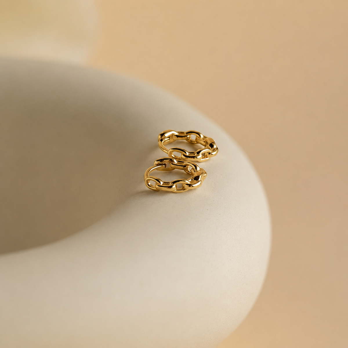 Gold chain earring on a beige ceramic dish with a beige background