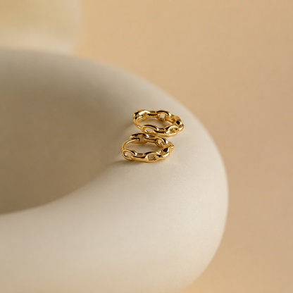 Gold chain earring on a beige ceramic dish with a beige background