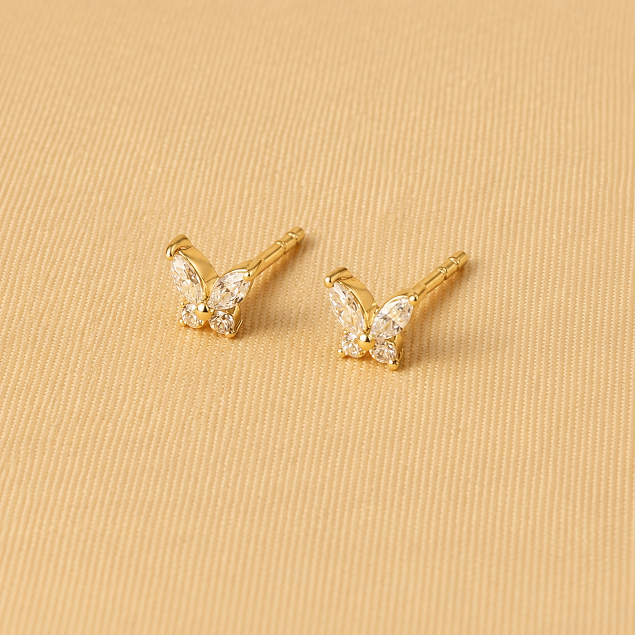 Gold butterfly earrings on a beige fabric background