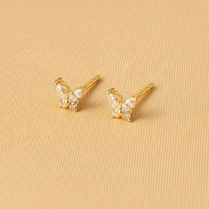 Gold butterfly earrings on a beige fabric background