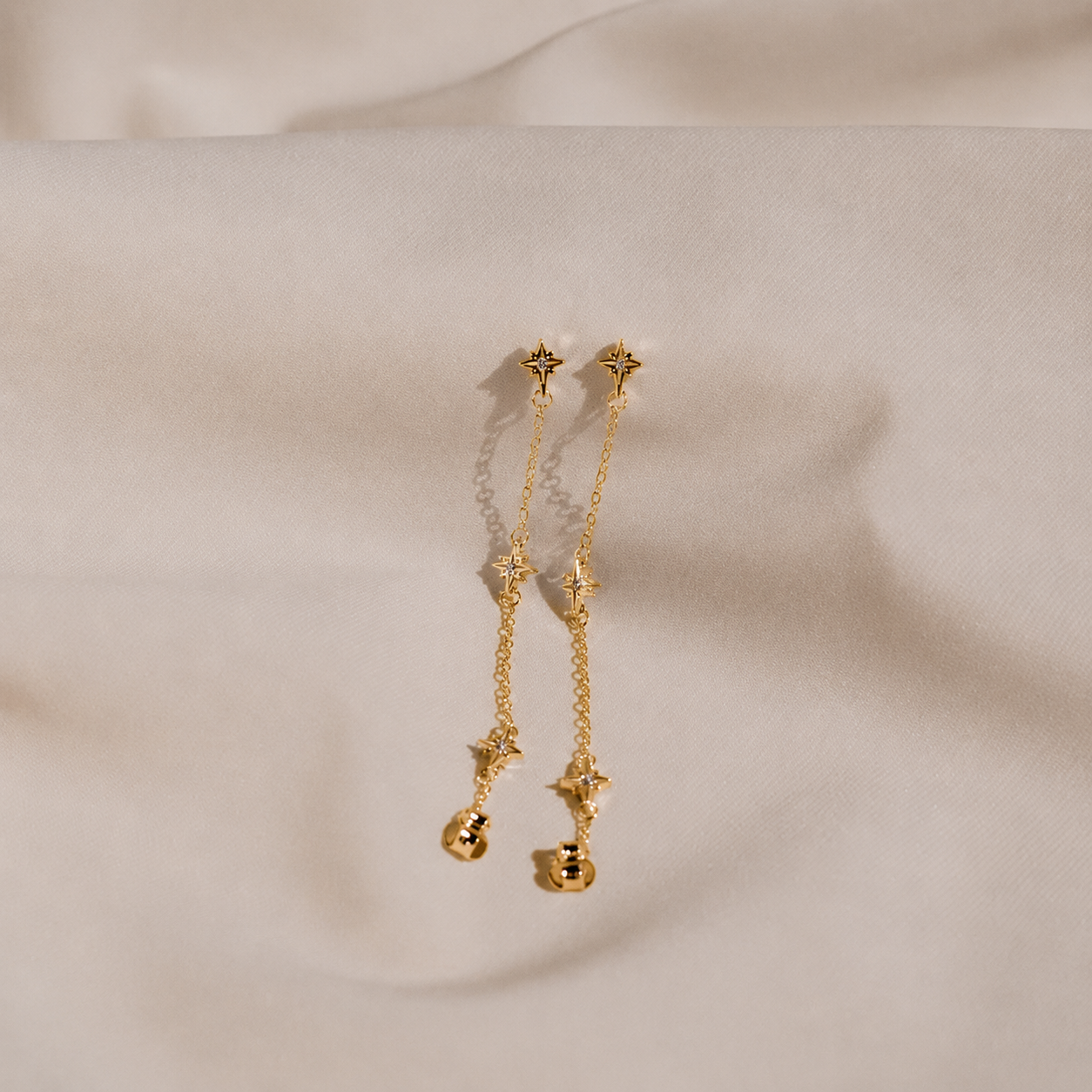 Gold earrings with star designs on a beige fabric background
