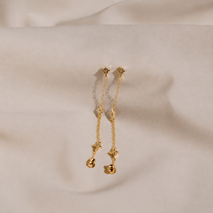 Gold earrings with star designs on a beige fabric background