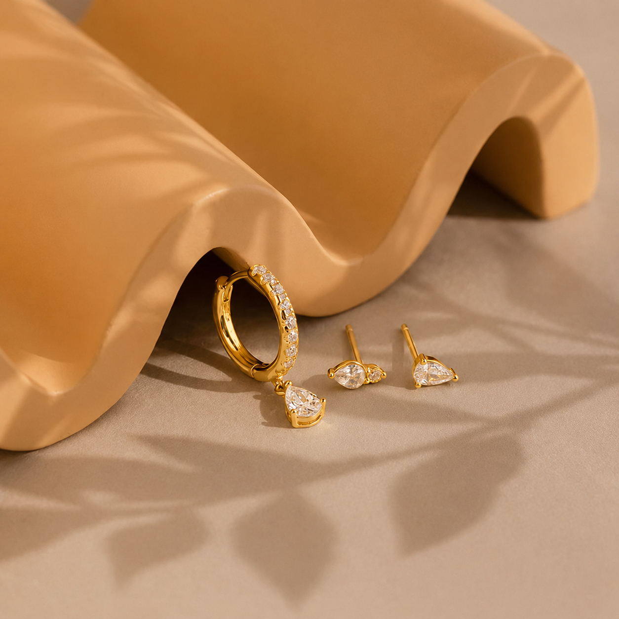 Gold earrings on a beige surface with a wavy beige object