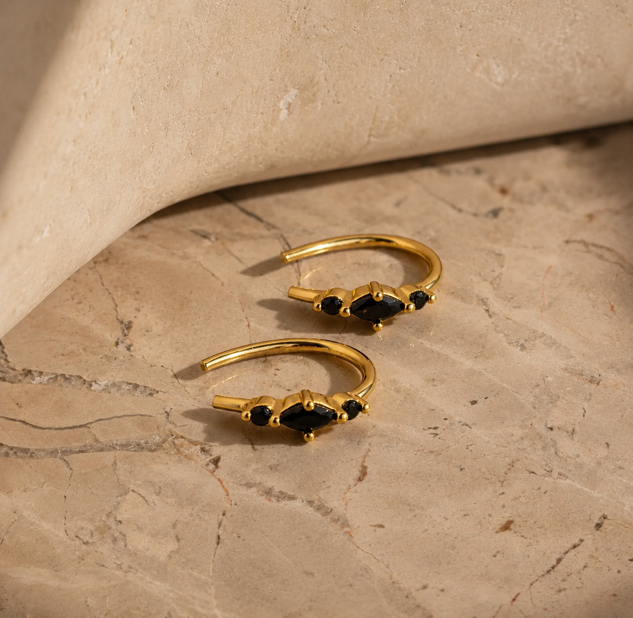 Gold hoop earrings with black gemstones on a beige marble surface