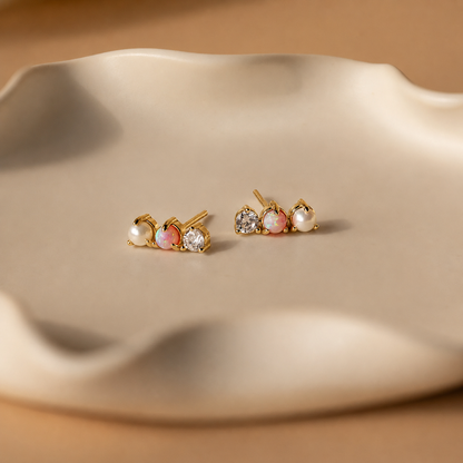 Pair of gold earrings with pearls and crystals on a beige surface