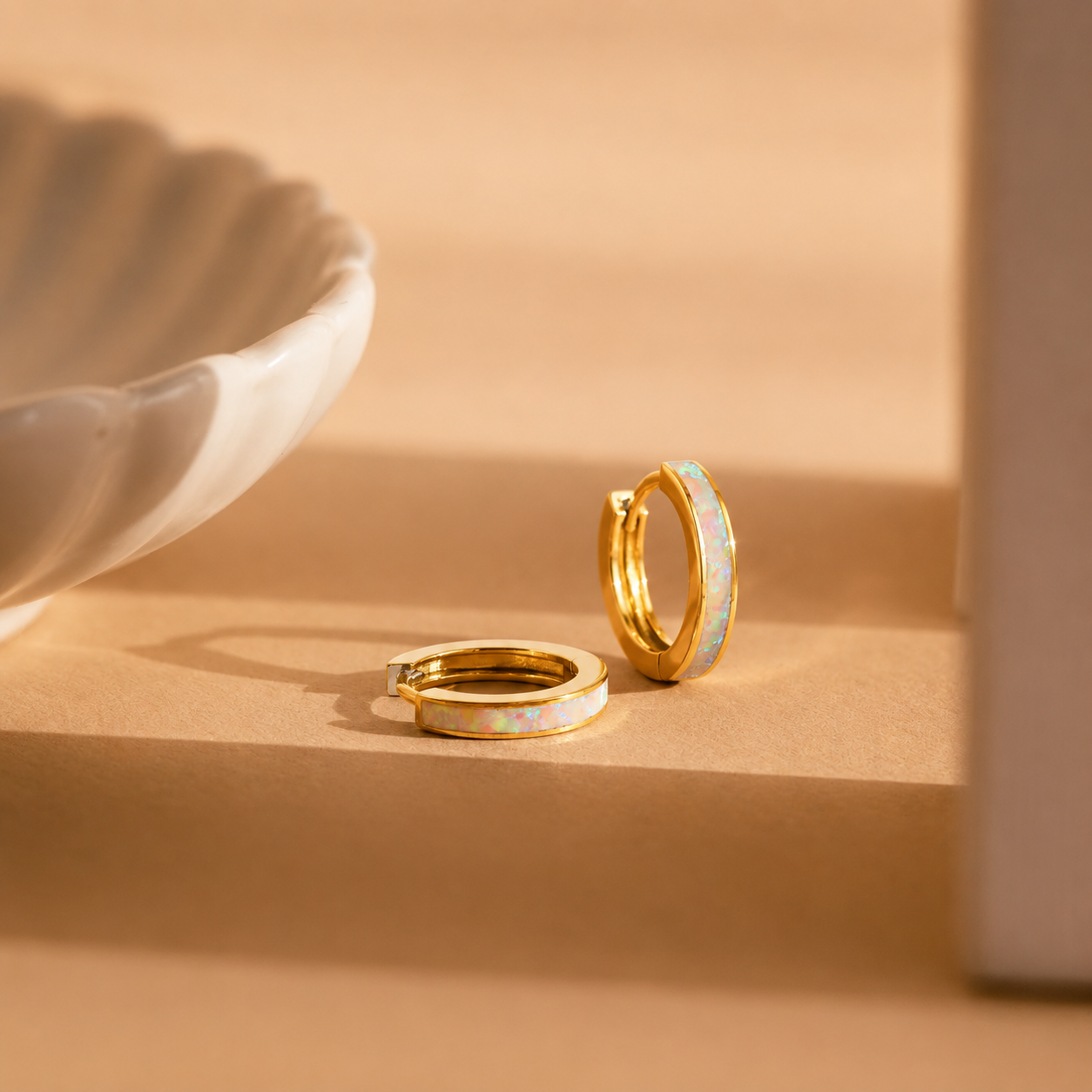 Two gold hoop earrings with opal inlay on a beige surface