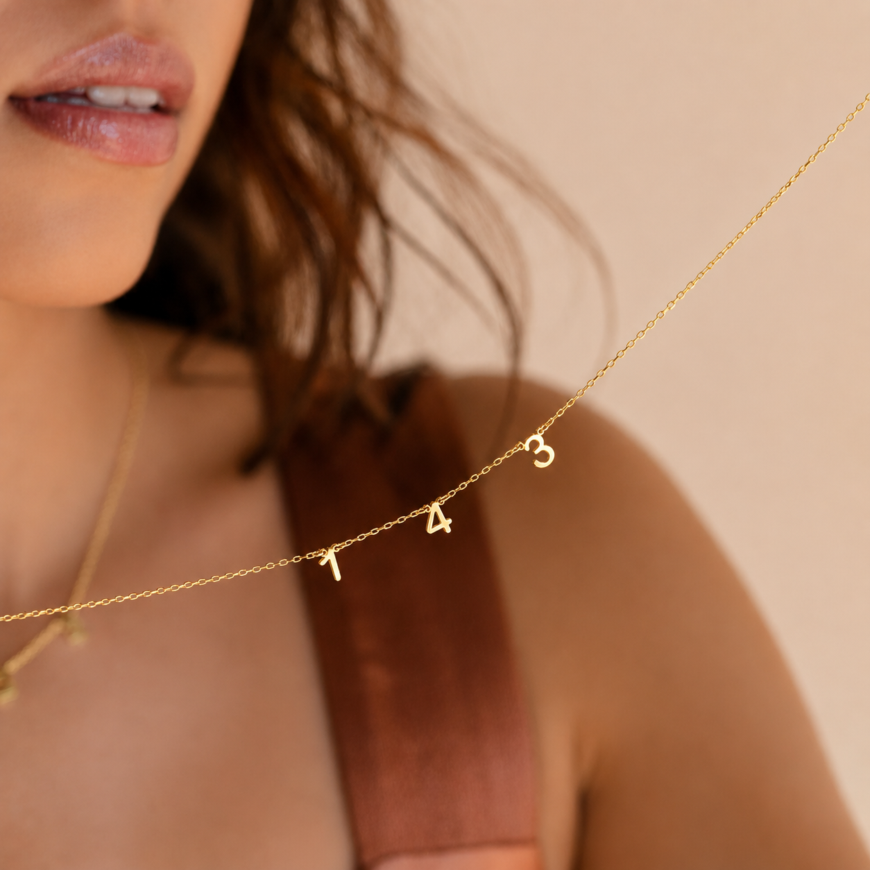 Close-up of a woman wearing a gold necklace with letter 'A' charms on a beige background