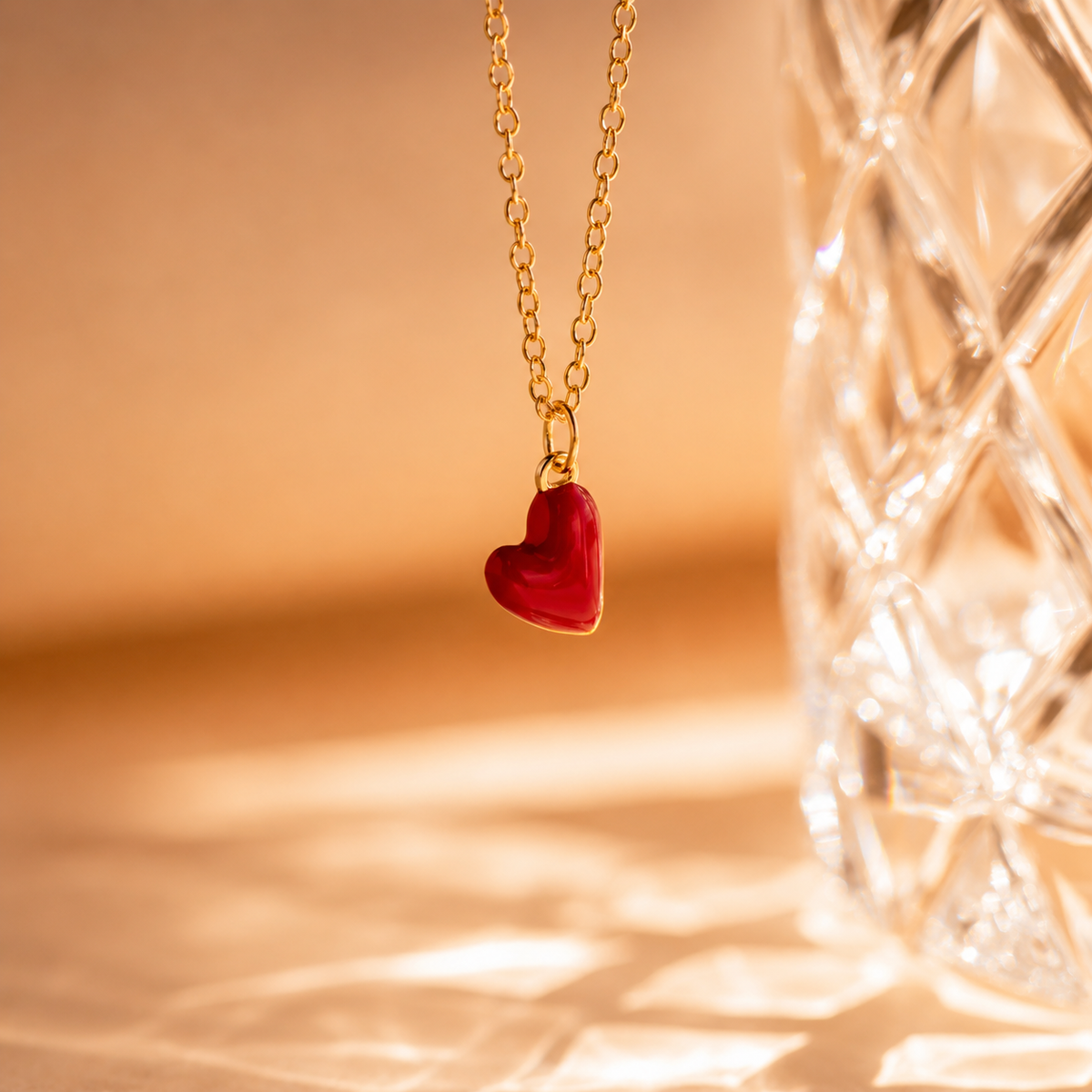 Gold necklace with a red heart pendant on a warm-toned background