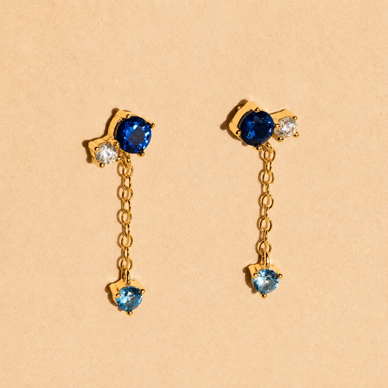 Gold earrings with blue gemstones on a beige background
