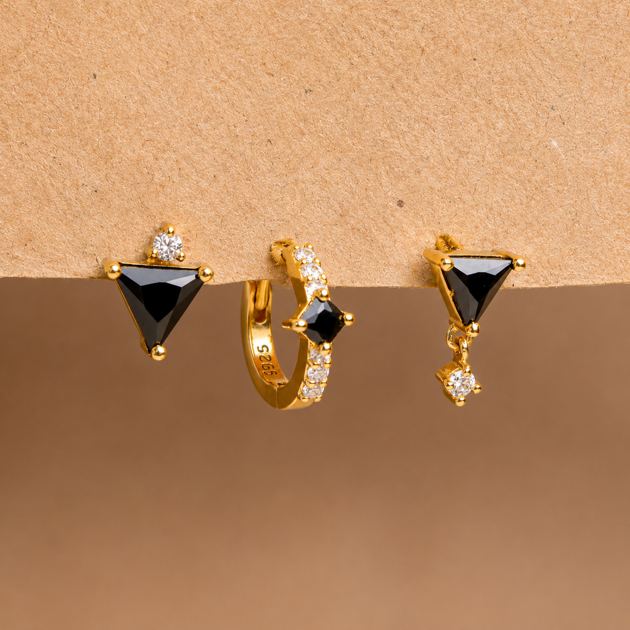 Three pairs of gold earrings with black gemstones on a brown background