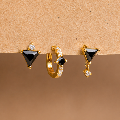 Three pairs of gold earrings with black gemstones on a brown background
