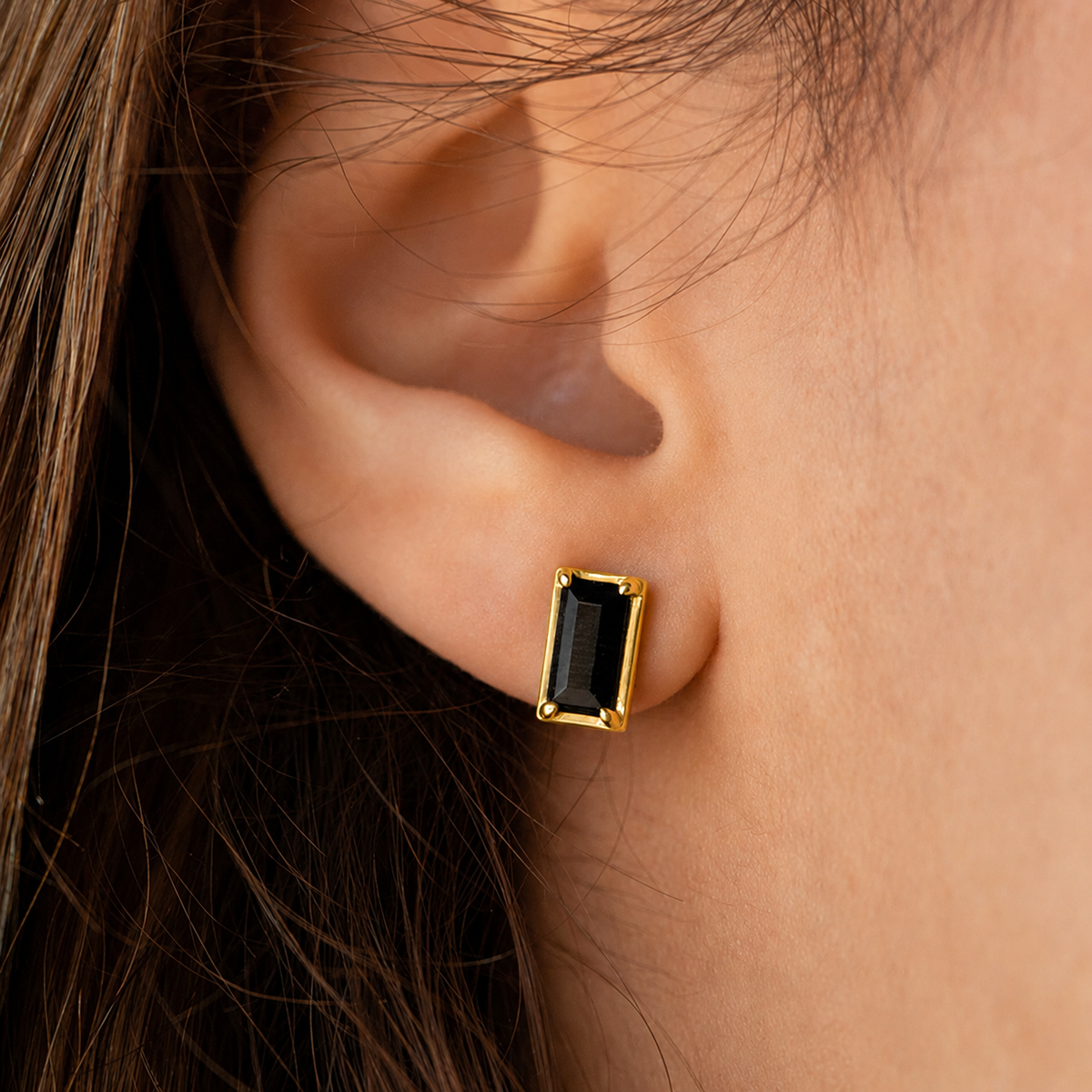 Gold earring with a black gemstone worn by a person