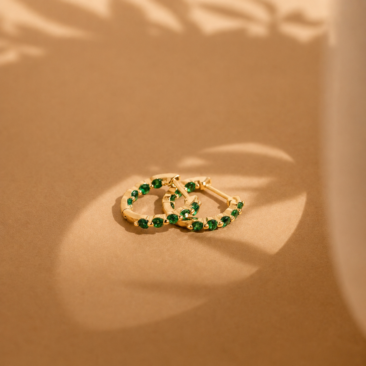 Gold hoop earrings with green gemstones on a beige background