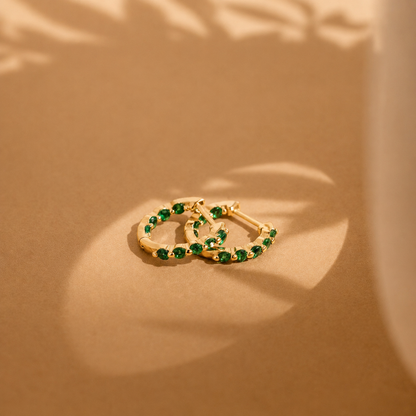 Gold hoop earrings with green gemstones on a beige background