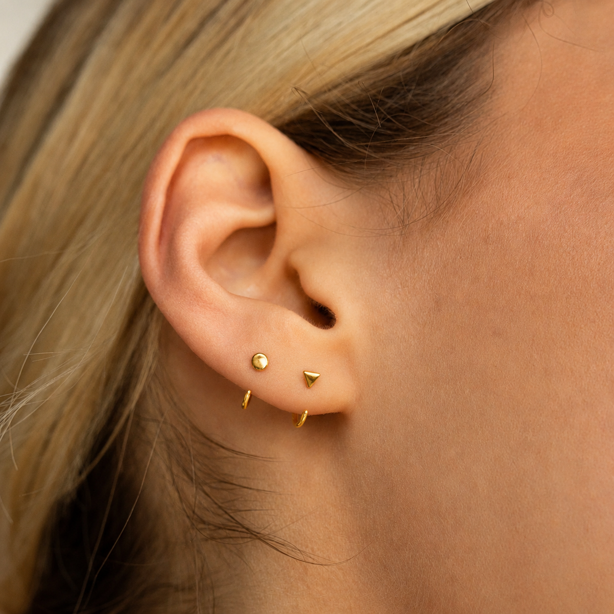 Close-up of an ear with gold earrings on a neutral background