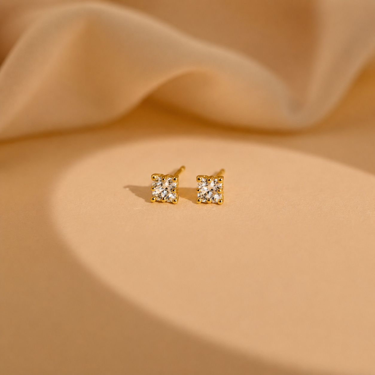 Gold square stud earrings on a beige fabric background
