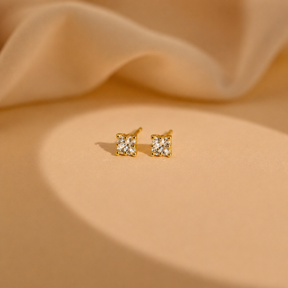 Gold square stud earrings on a beige fabric background