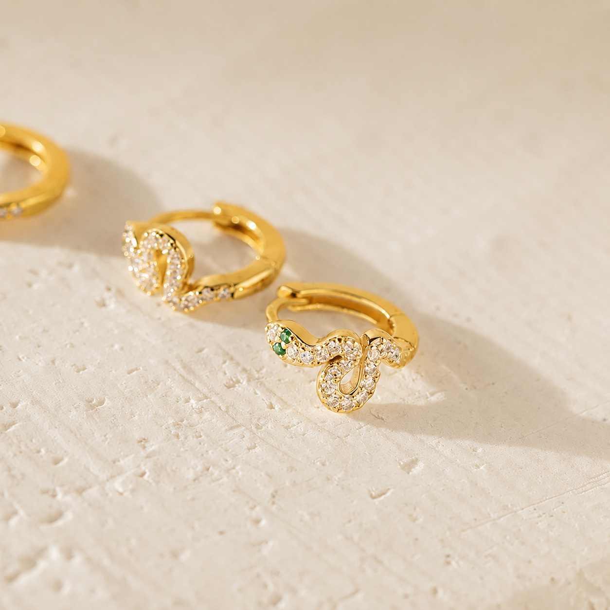 Gold hoop earrings with gemstones on a textured beige surface