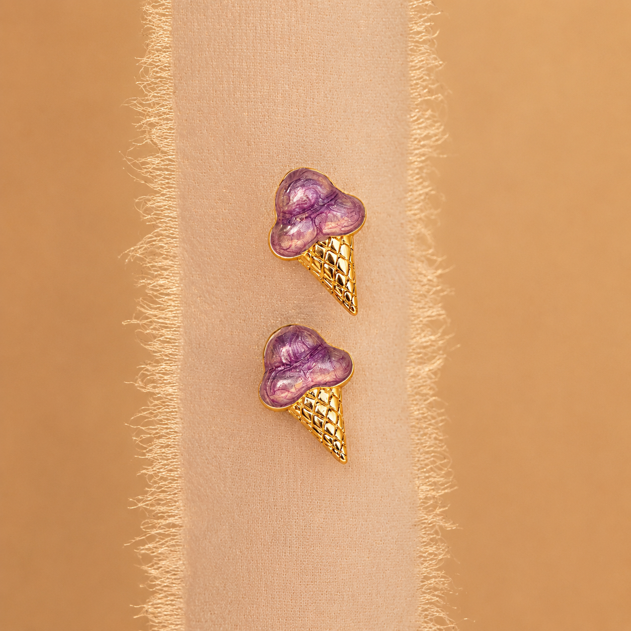 Purple heart-shaped ice cream cone earrings on a beige fabric background