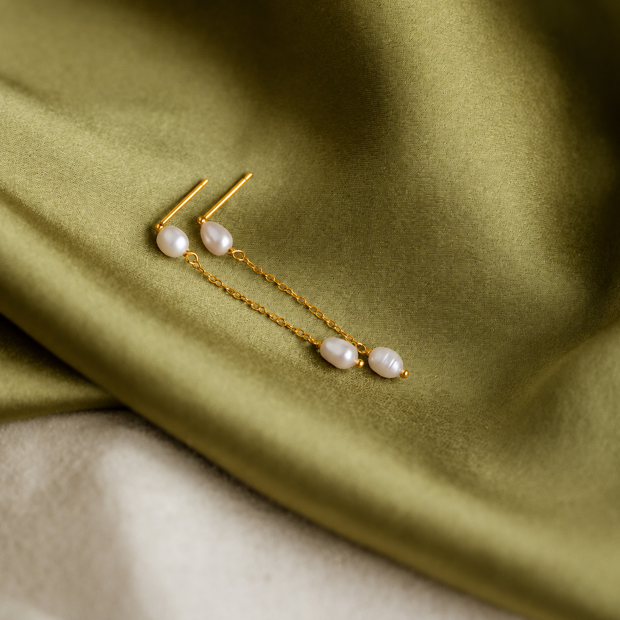 Gold earrings with pearls on a green fabric background