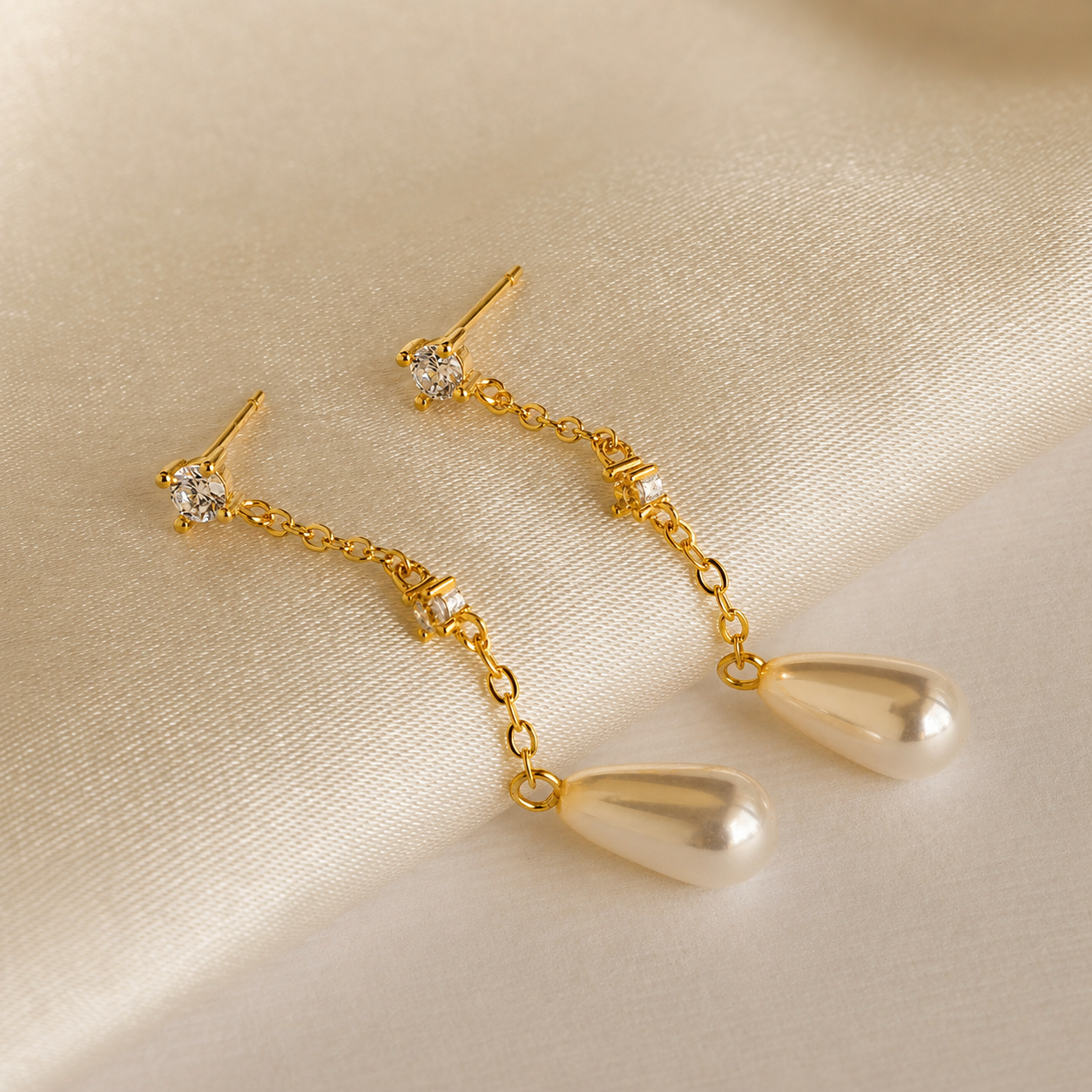 Gold earrings with teardrop-shaped pendants on a beige fabric background