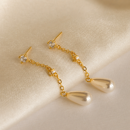 Gold earrings with teardrop-shaped pendants on a beige fabric background