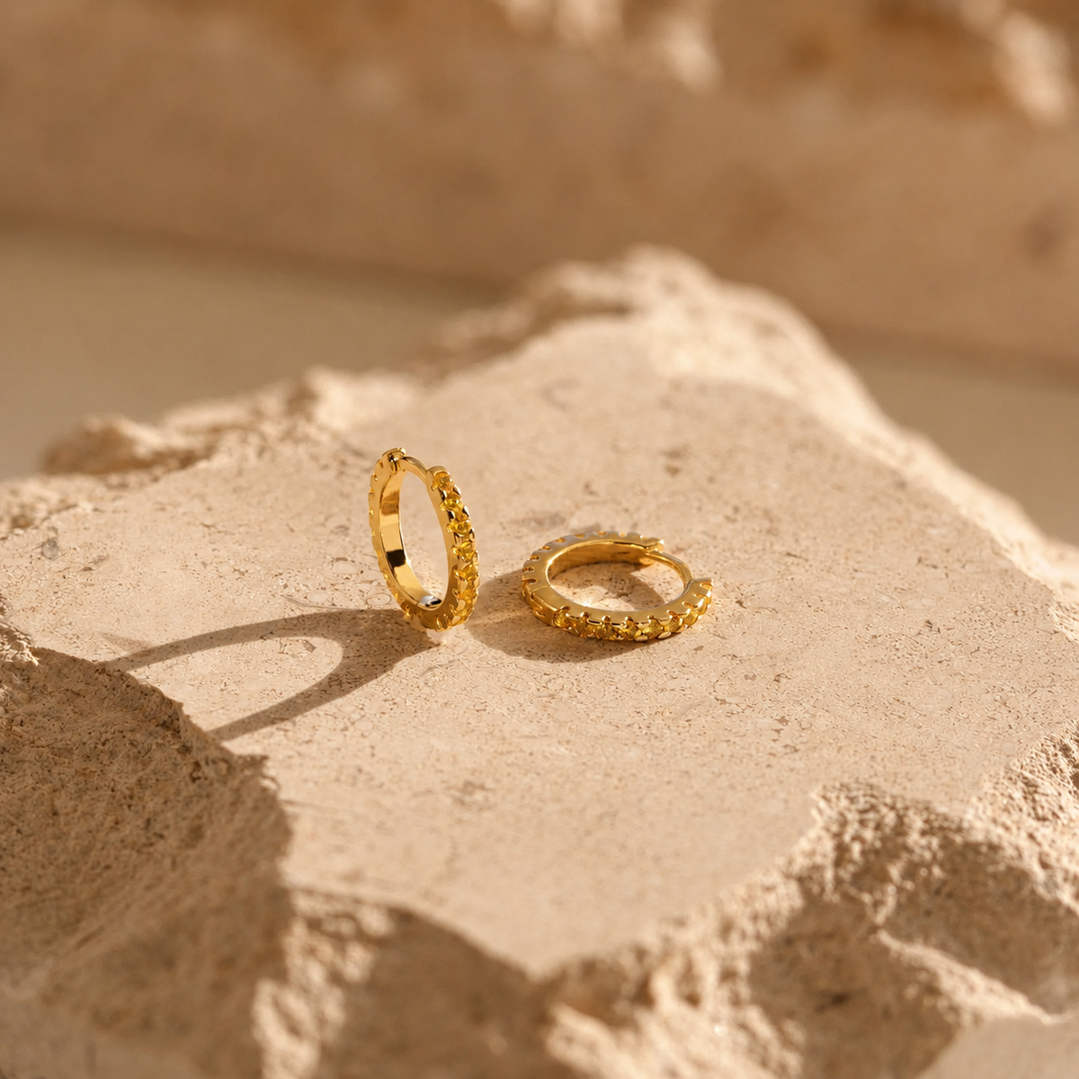 Two gold hoop earrings on a textured beige surface