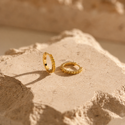 Two gold hoop earrings on a textured beige surface