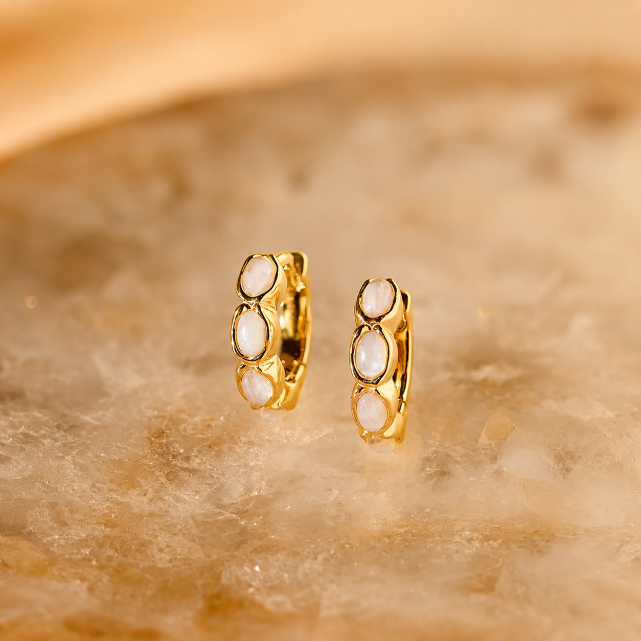 Gold hoop earrings with embedded stones on a gold marble background