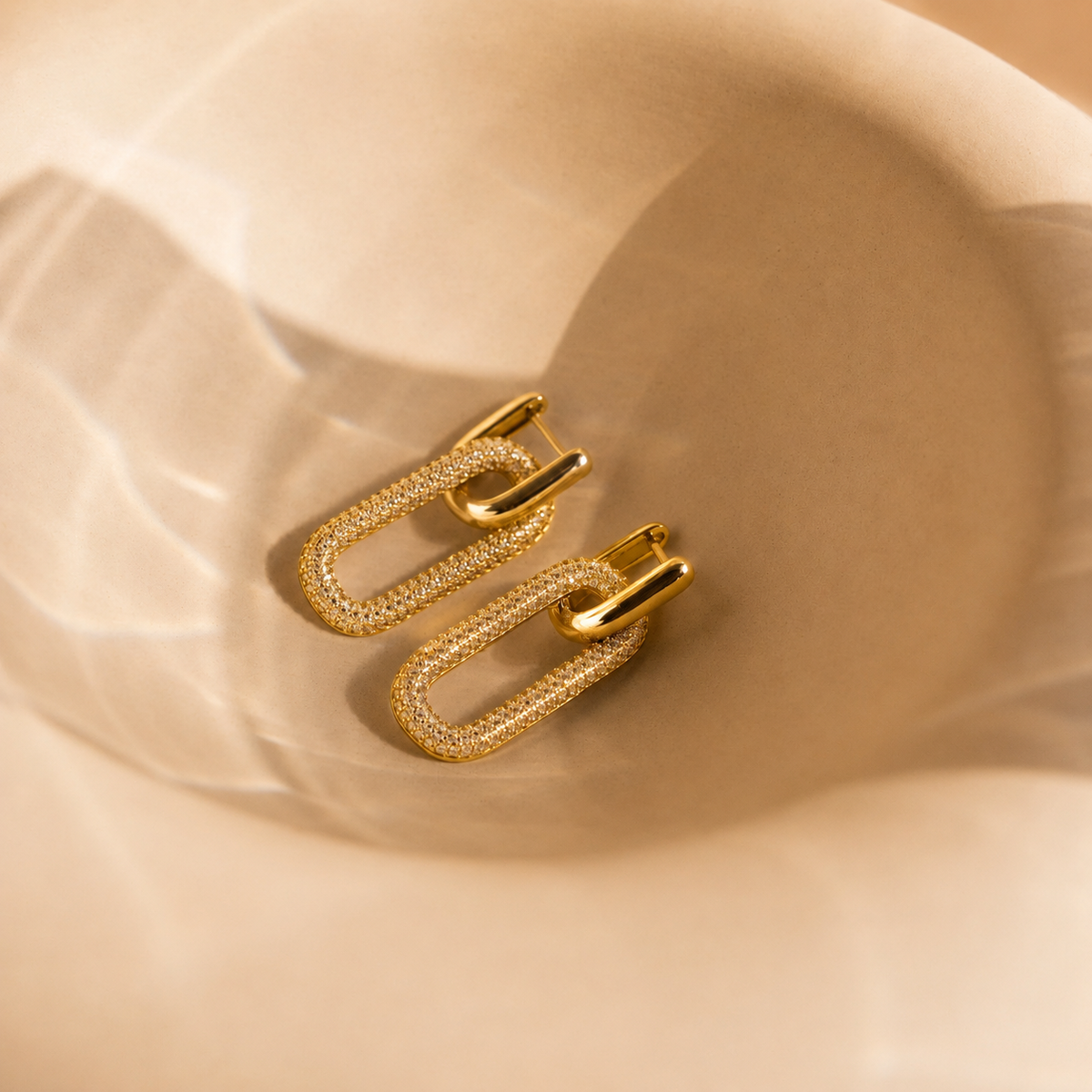 Gold chain-style earrings on a beige fabric background