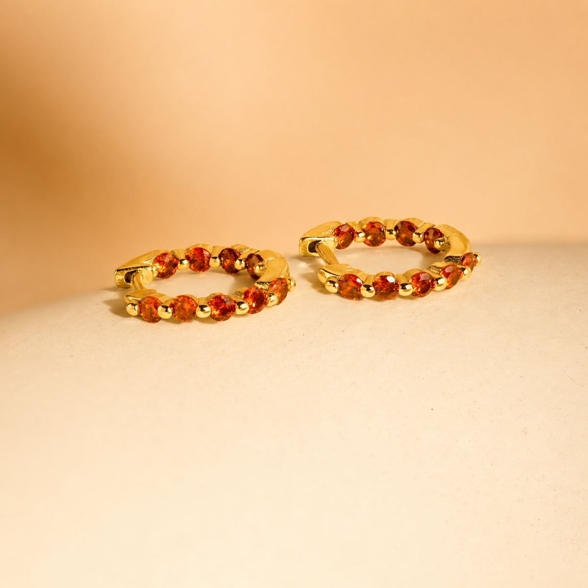 Gold hoop earrings with orange gemstones on a beige background