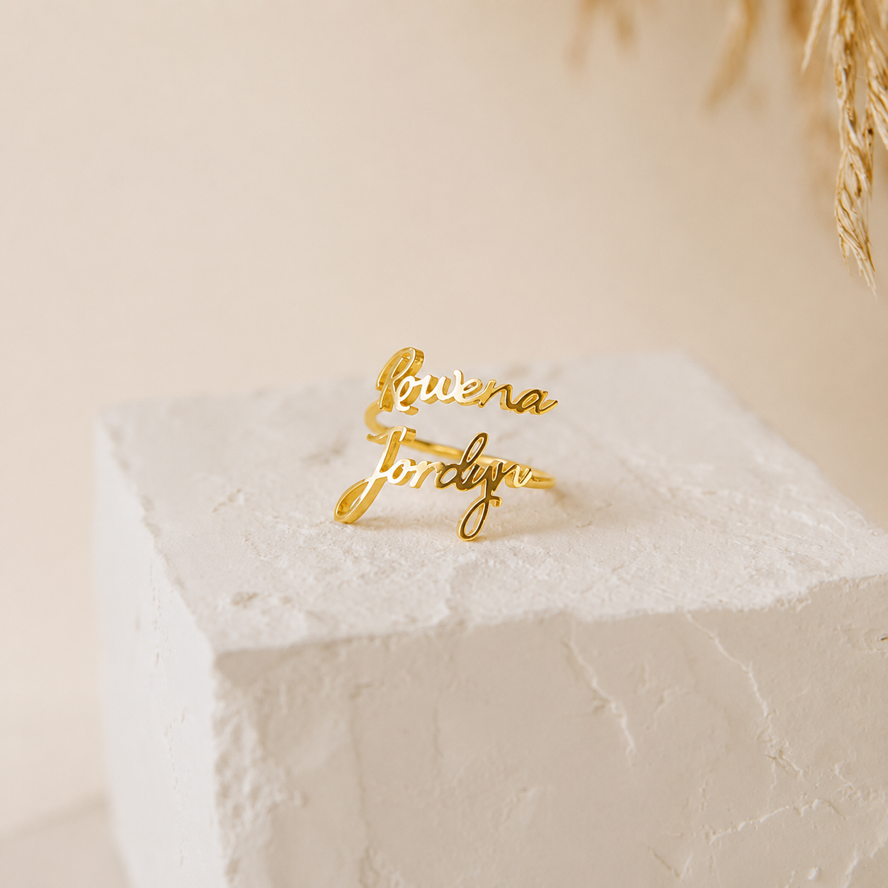 Gold name ring on a textured white surface with a neutral background