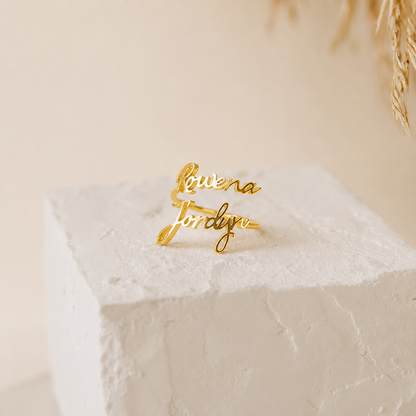 Gold name ring on a textured white surface with a neutral background