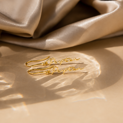 Gold earrings on a beige fabric background