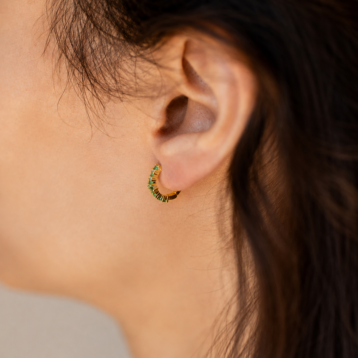 Close-up of an ear wearing a green and gold hoop earring.