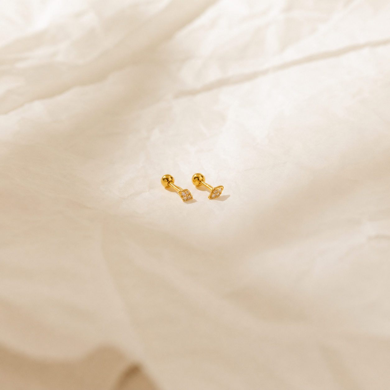 Gold dumbbell-shaped earrings on a beige fabric background