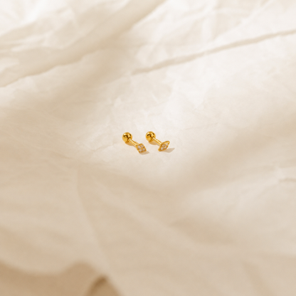 Gold dumbbell-shaped earrings on a beige fabric background