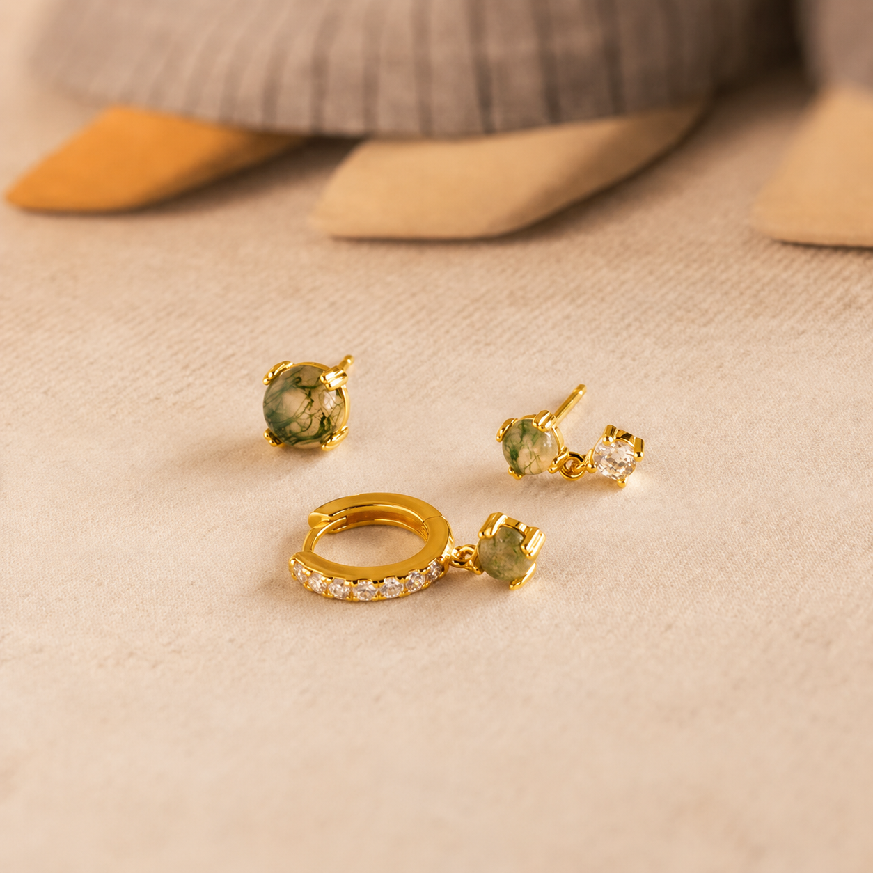 Gold jewelry set with green gemstones on a beige surface