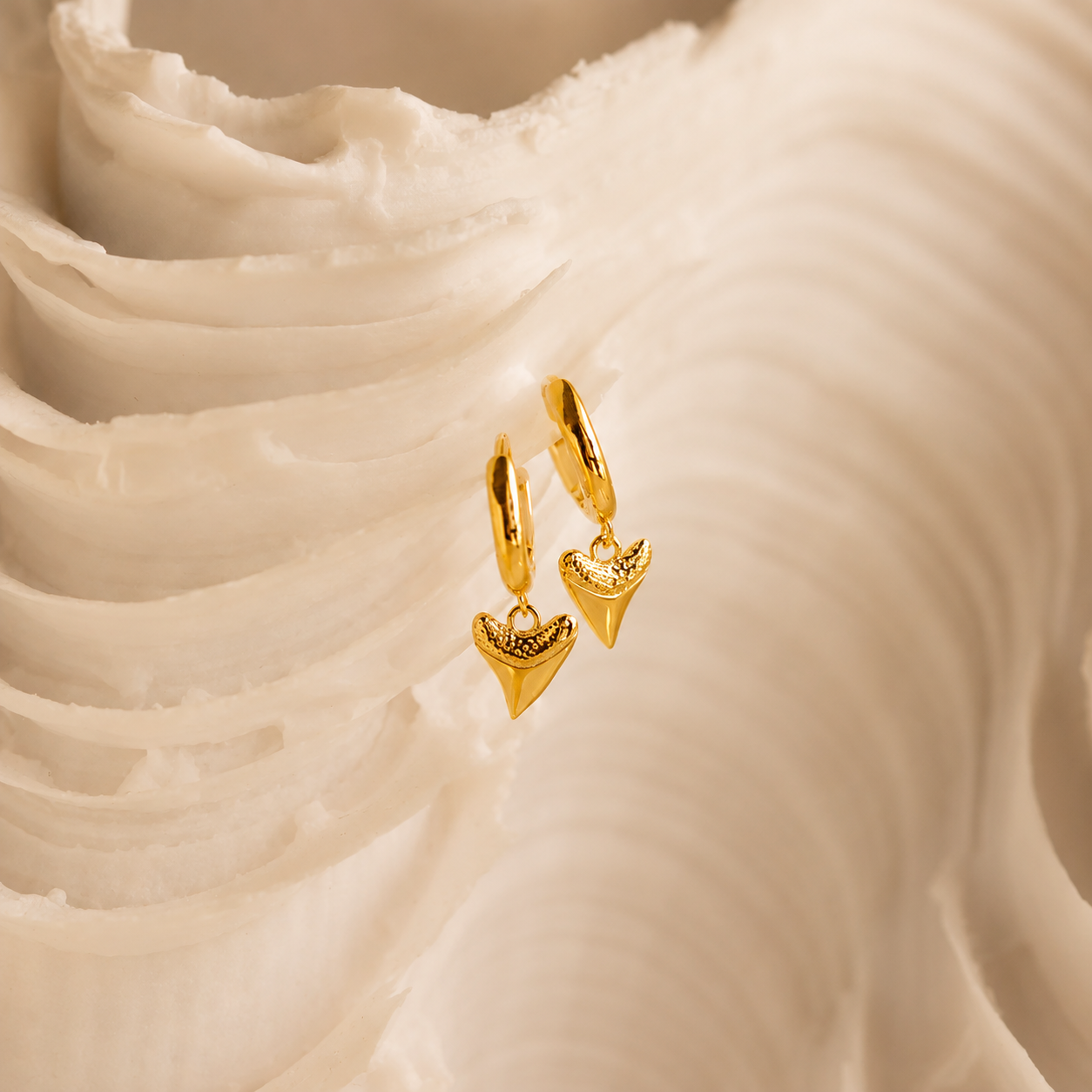 Gold hoop earrings with heart-shaped charms on a textured beige surface
