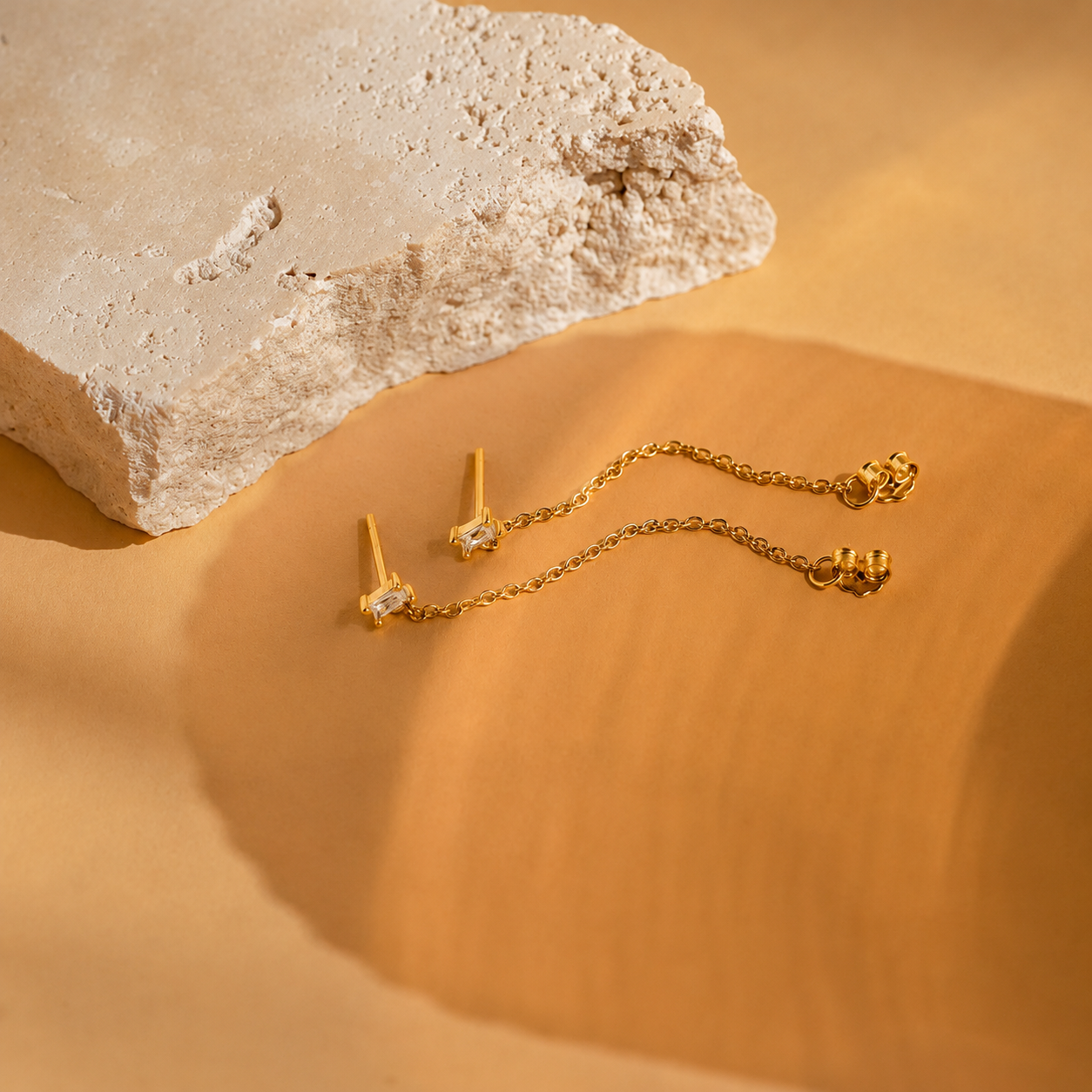Gold earrings on a textured beige surface with a rock in the background