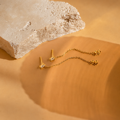 Gold earrings on a textured beige surface with a rock in the background